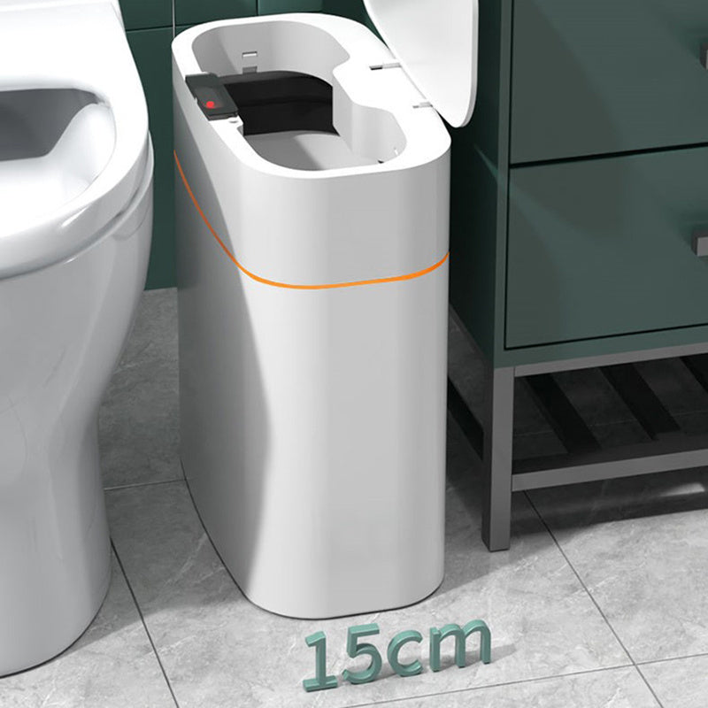 Smart trash can with touchless lid, designed for compact spaces, next to a toilet in a modern bathroom.